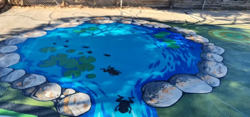 Waterhole mural with lily pads frogs and painted stones on asphalt